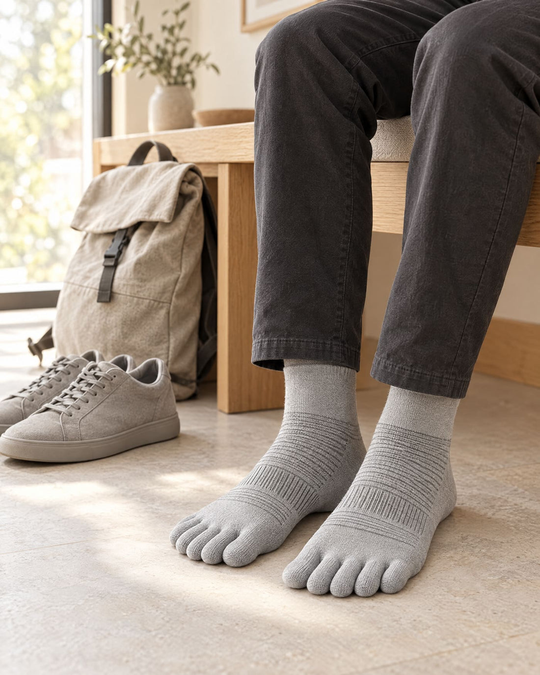 Persona sentada en un banco de casa con calcetines de cinco dedos y unas zapatillas al lado